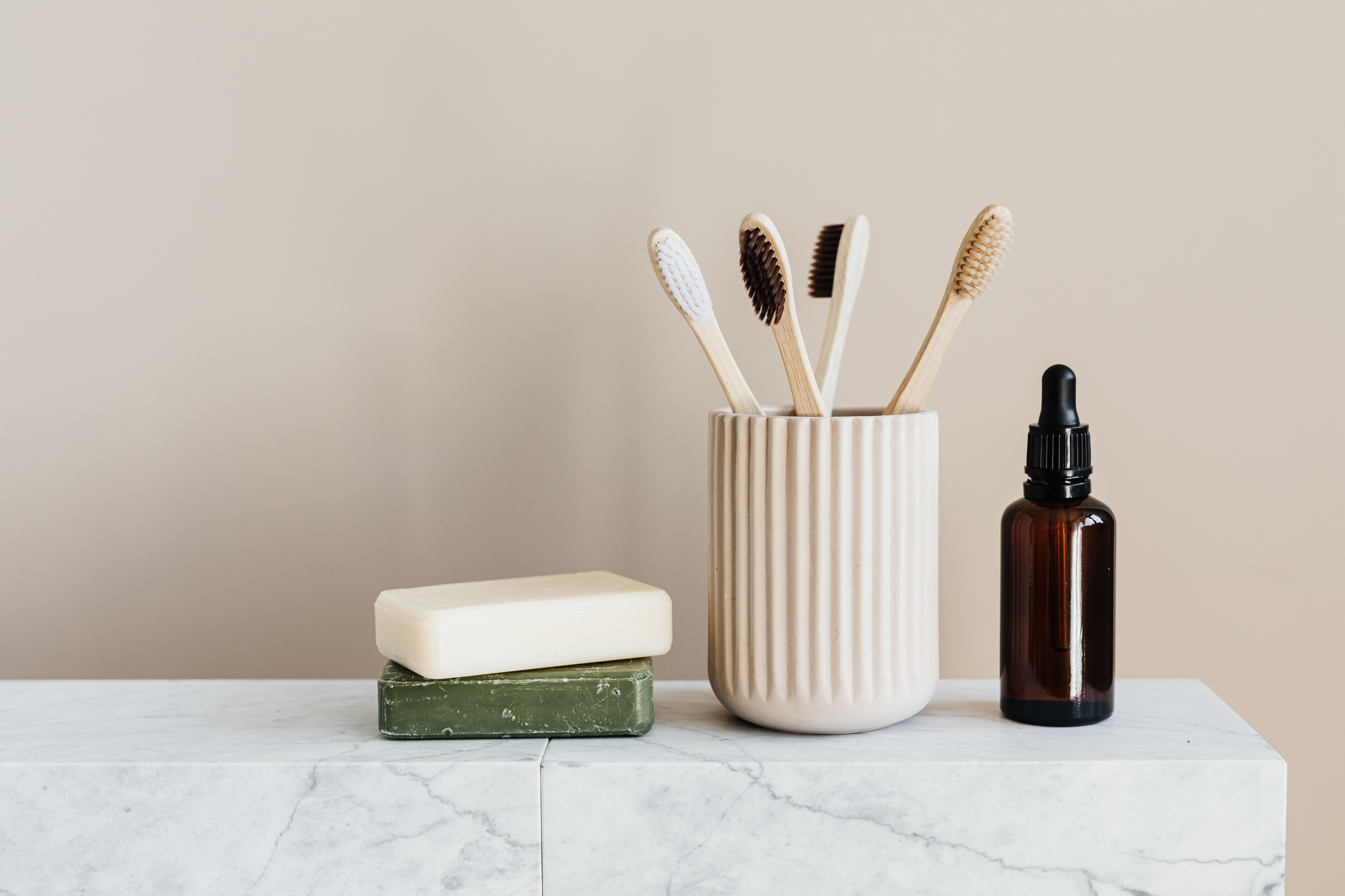 Free Collection of organic soaps and bamboo toothbrushes in ceramic minimalism style holder placed near renewable glass bottle with essential oil on white marble tabletop against beige wall